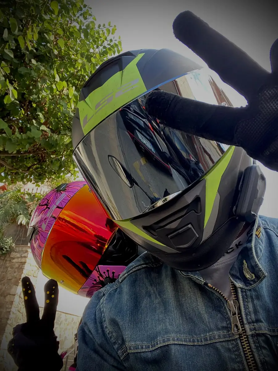 Javier con el casco de la moto puesto, la visera ahumada y el signo de la paz, con un segundo casco en la mano